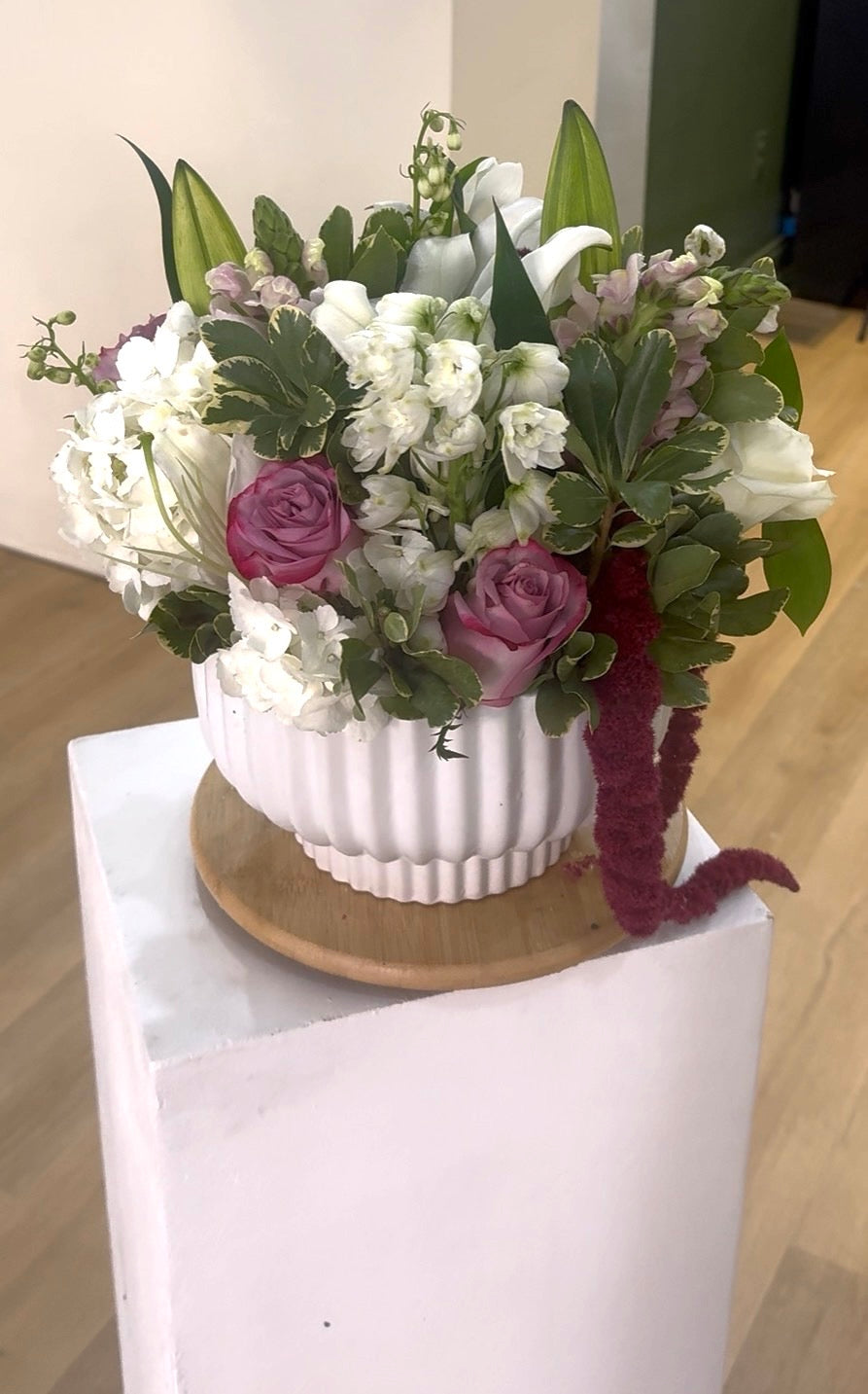Floral arrangement with white and purple flowers in a white pot on a white pedestal.